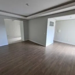 Foto interna de uma sala com piso de madeira.