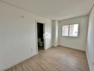 Interior de uma sala com piso de madeira clara e porta de acesso a um banheiro.