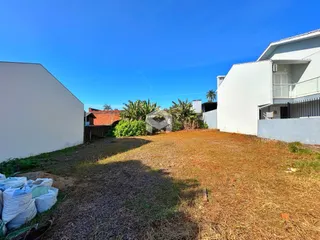 Vista externa de um terreno com grama seca entre duas construções brancas.