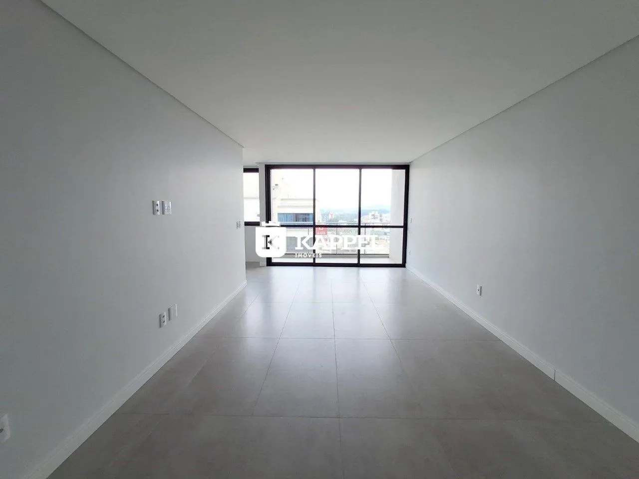 Hall de corredor longo com paredes brancas e grande janela.