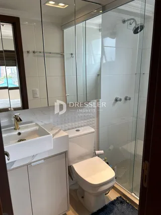 Foto de um banheiro com box de vidro e louças brancas.