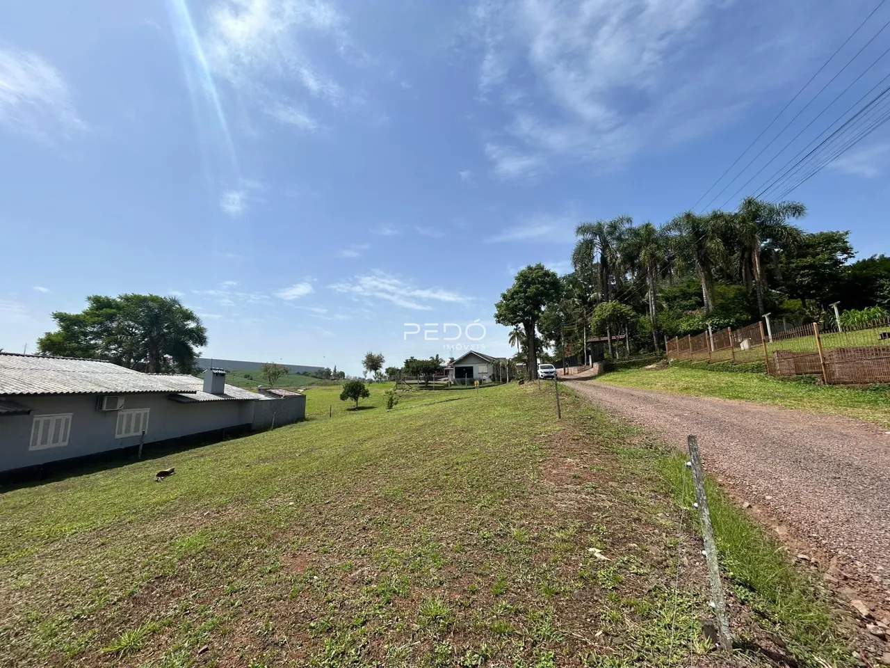 Vista da propriedade rural em Lajeado, Brasil, mostrando um campo gramado e uma estrada de terra.