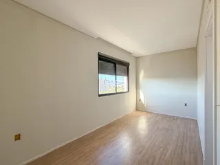 Vista interna de uma sala com paredes brancas e piso de madeira clara.