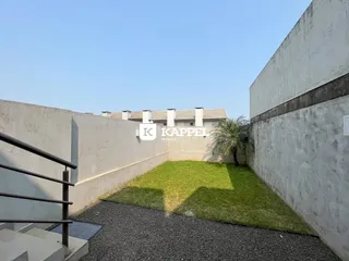 Vista externa mostrando um gramado e muros de concreto em uma propriedade.