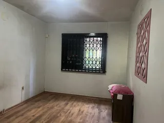 Um cômodo interno com piso de madeira e janela com grade de ferro.