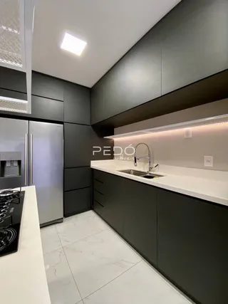 Vista da cozinha moderna com armários escuros e bancadas brancas.