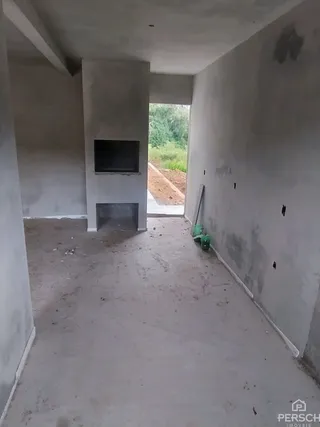 Ambiente interno com paredes brancas e piso de concreto, mostrando uma área sem acabamento.