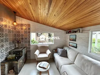 Sala de estar com sofá, poltrona e lareira em ambiente com teto de madeira.