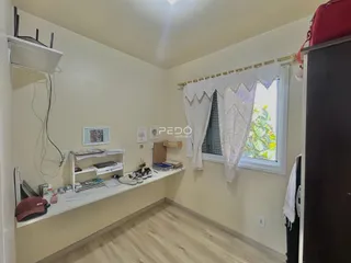 Ambiente interno de uma sala com piso de madeira clara e janela decorada.