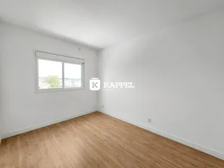 Uma sala de estar vazia com piso de madeira clara e uma janela.