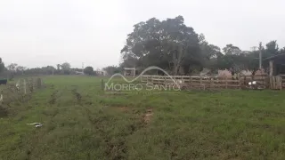 Vista externa de um campo gramado com cerca de madeira e vegetação ao fundo.