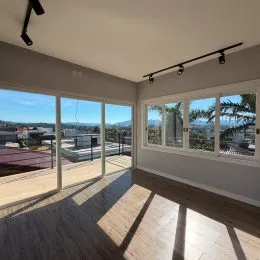 Vista panorâmica da sala com piso de madeira e grandes janelas.