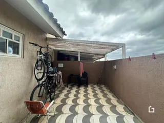 Vista externa de um pátio pavimentado adjacente a uma parede de uma residência.