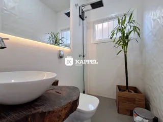 Banheiro com bancada de madeira, pia de apoio e vaso sanitário.