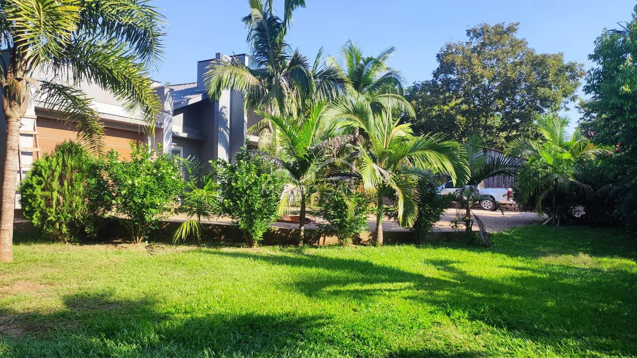 Fachada da residência com gramado verde e vegetação tropical.