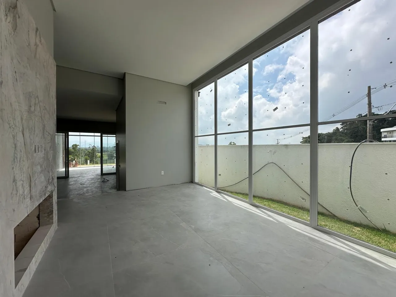 Ambiente interno com piso de concreto e grandes janelas que dão vista para o exterior.