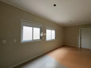 Vista interna de um ambiente com piso de madeira e duas janelas.