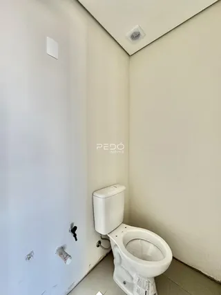 Vista do canto de um banheiro com vaso sanitário e tubulações expostas.