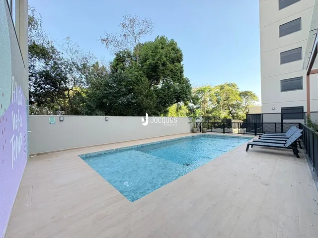A foto exibe uma piscina externa com deck e área verde ao lado de uma parede.