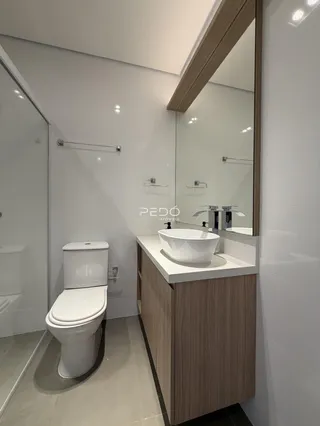 Banheiro moderno com louças brancas e armários de madeira clara.