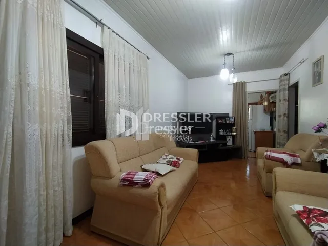 Sala de estar com sofá claro e cortinas brancas em um imóvel no Brasil.