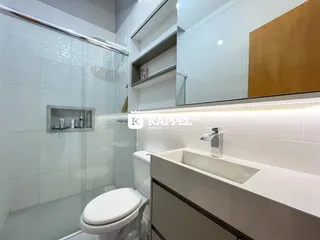 Banheiro com box de vidro, vaso sanitário e bancada de pia.