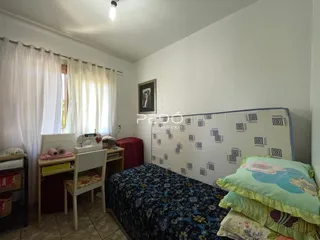 Quarto com cama e janela com cortinas brancas.