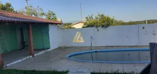 Foto externa mostrando uma piscina com um muro branco em uma propriedade.