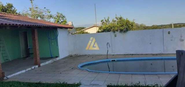 Foto externa mostrando uma piscina com um muro branco em uma propriedade.