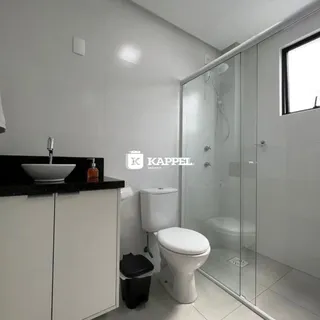 Banheiro com box de vidro e louças brancas.