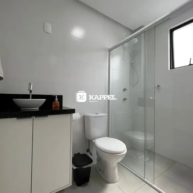 Banheiro com box de vidro e louças brancas.