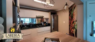 Vista interna de uma cozinha moderna com armários brancos e bancada de madeira.