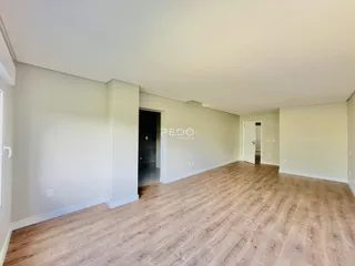 Interior de uma sala ampla com piso de madeira clara.