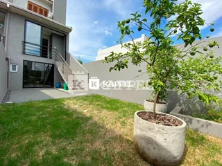 Vista externa mostrando um jardim com gramado e uma árvore em vaso.
