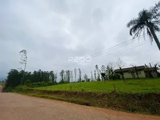 Vista externa de uma propriedade rural com campo gramado e vegetação ao fundo.