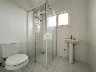 Banheiro com box de vidro e piso cerâmico branco.