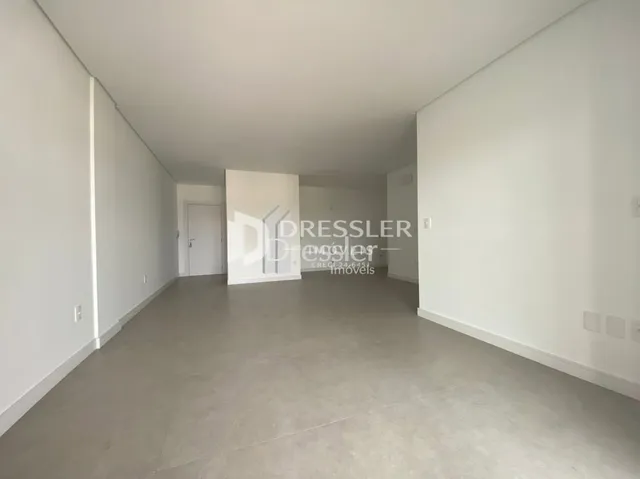 Ambiente interno de um espaço vazio com paredes brancas e piso cinza.