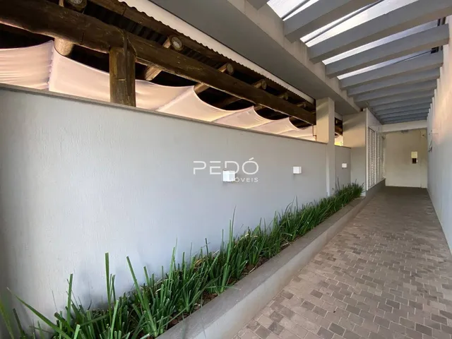 Corredor interno com revestimento de parede branca e jardim lateral.