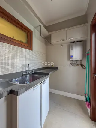 Vista interna de uma cozinha com bancada e armários brancos.