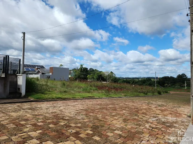 Vista externa de uma propriedade com calçamento de tijolos e vegetação ao fundo sob um céu nublado.