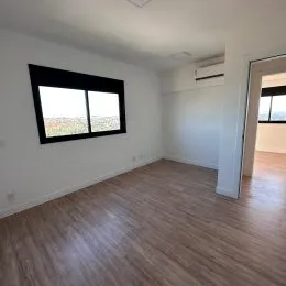 Ambiente interno com piso de madeira e janela mostrando a paisagem externa.