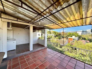 Varanda com piso de ladrilhos vermelhos e vista para a vegetação.