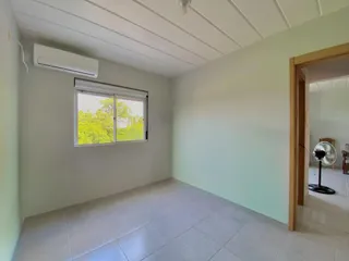 Uma sala de estar clara com piso de cerâmica e janela para a vegetação externa.