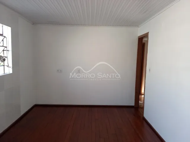 Foto de um cômodo interno com piso de madeira escura e paredes brancas.