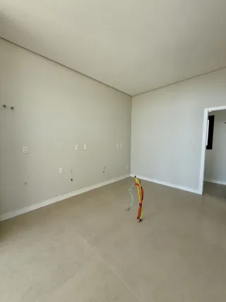 Sala ampla e vazia com paredes brancas e piso claro.