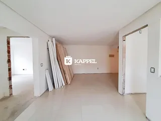 Interior de uma sala em construção com paredes brancas e tábuas de madeira expostas.