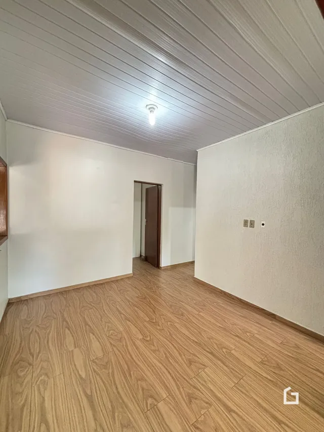 Interior de uma sala com piso de madeira clara e paredes brancas.