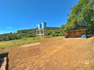 Vista da propriedade com vegetação e estruturas rústicas sob um céu azul.
