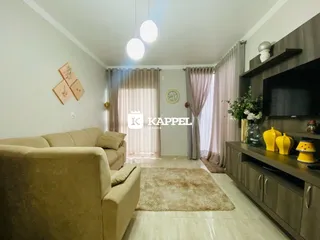 Sala de estar com sofá e painel de TV na parede, com cortinas claras.