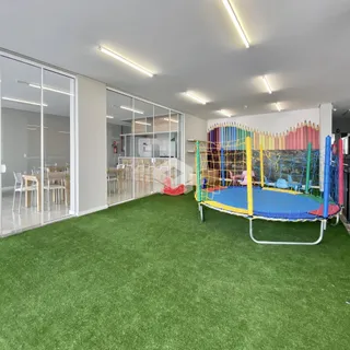 Espaço interno com piso de grama sintética e estrutura de playground.